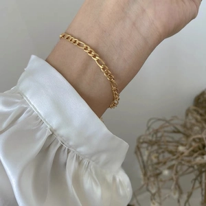 Elegant women's gold Figaro chain bracelet featuring alternating bead links on wrist