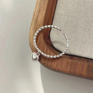 Detail of S925 sterling silver twist ring with a heart-shaped pendant on wooden tray