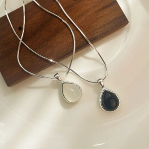 Detail of silver drop-shaped necklaces with black and white pendants on a wood block