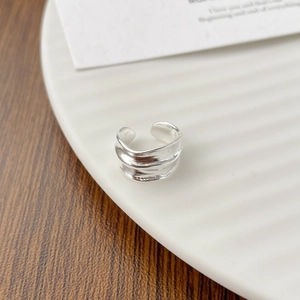 Top view detail of an irregular triple-layer silver wave ring on a white ceramic plate