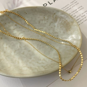 Detailed view of golden double-layer necklace with flat disc chain and cross O-chain
