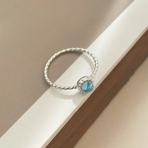 Gros plan sur une bague torsadée en argent S925 sertie d'un cristal bleu rond poli