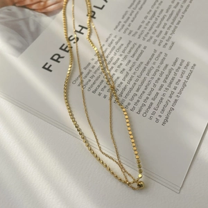 Detail of a minimalist 18K gold double-layer necklace with chic flat disc and beads