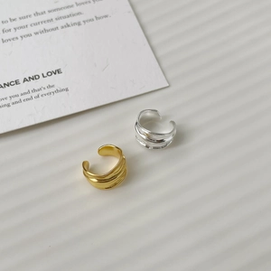 Macro detail of gold and silver irregular wave ear cuffs on a minimalist white background