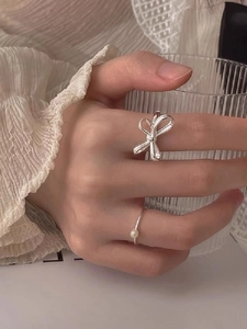 Macro shot of silver bow ring and minimalist pearl ring on hand holding a glass