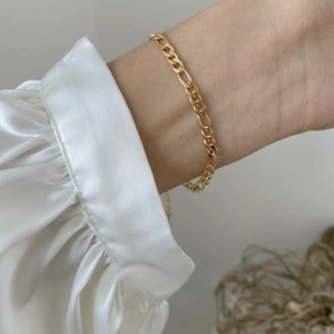 Close-up of elegant gold Figaro chain bracelet worn over white satin silk sleeves