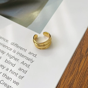 Close-up of golden wavy textured ear cuff with irregular liquid metal design on book