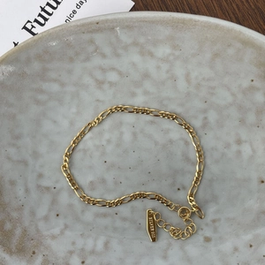 Close-up of S925 sterling silver stamp on golden Figaro chain bracelet on ceramic tray