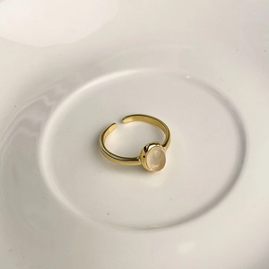 Detailed macro view of an adjustable gold-plated ring with an oval pink-white gemstone