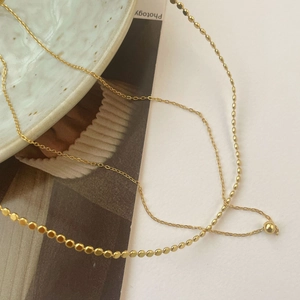 Detailed close-up of double-layer gold S925 silver necklace with bead and ball pendants