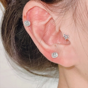 Gros plan de boucles d'oreilles S925 argent massif smiley et étoile portées à l'oreille