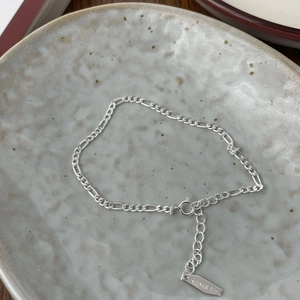 Detailed close-up of polished S925 sterling silver Figaro chain with lobster clasp and tag