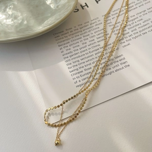 Close-up of golden S925 sterling silver layered necklace with small disc charms on paper
