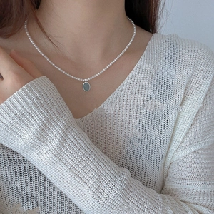 Close-up of S925 silver pearl necklace with oval green pendant on white sweater