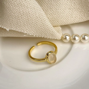 Detail of an adjustable gold ring with an oval chalcedony stone on a white ceramic tray