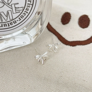 Détail de boucles d'oreilles nœud papillon en argent S925 sur un tissu crème minimaliste