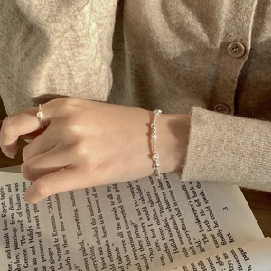 Détail d'un bracelet à breloques cœur et d'une bague perle portés en lisant un livre