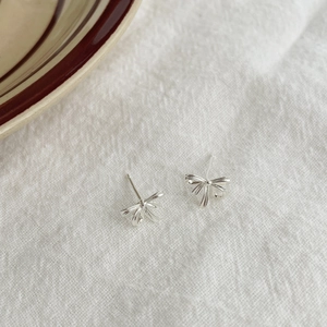 Détail de boucles d'oreilles nœud en argent avec texture ruban sur fond de lin blanc