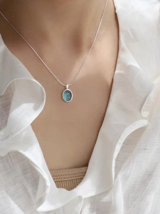 Detailed close-up of a blue oval gemstone pendant on a silver snake chain for women