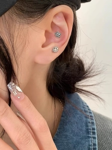Détail de boucles d'oreilles S925 en argent avec motif sourire et fleur sur l'oreille