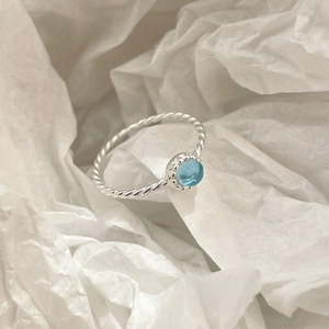 Gros plan d'une bague tressée en argent S925 sertie d'un cristal bleu ciel poli
