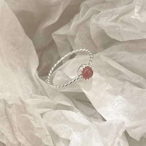 Macro d'une bague tressée en argent S925 avec pierre de cristal rose sur papier blanc