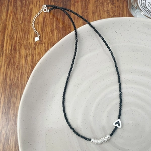Détail macro d'un collier de perles noires avec un pendentif cœur argenté et chaînette