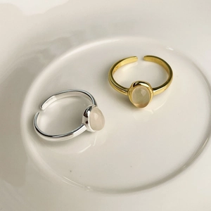 Close-up of gold and silver S925 rings with oval chalcedony on white ceramic plate