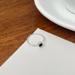 Détail macro d'une bague tressée en argent S925 avec une pierre noire ronde sertie en couronne