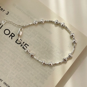 Détail du bracelet en argent S925 avec cœurs et perles argentées sur un vieux livre