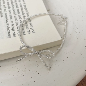 Close-up of S925 silver beaded bracelet with bow accent on an open book background
