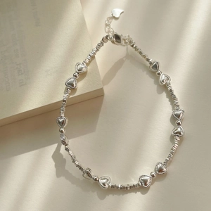 Détail d'un bracelet en perles de cœur argentées avec fermoir ajustable sur un fond épuré