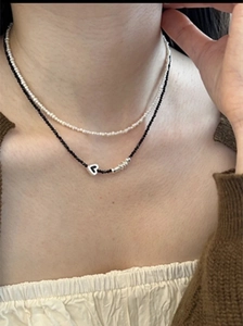 Détail d'un collier double épaisseur avec perles noires et blanches et pendentif cœur argenté