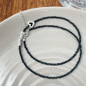 Détail du collier de perles facettées noires avec pendentif coeur argenté sur plat