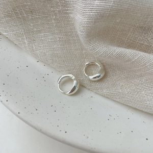 Polished S925 sterling silver huggie earrings on a minimalist ceramic tray
