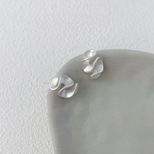 Dettaglio macro di orecchini a balze in argento opaco con trama a pieghe irregolare