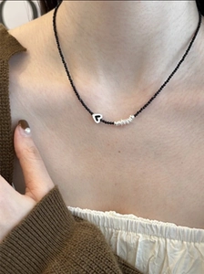 Détail d'un collier ras du cou en perles noires avec un pendentif cœur argenté sur modèle