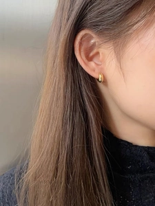 Detailed close-up of golden teardrop earring worn by a model in minimalist modern style