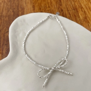 Detail of S925 sterling silver bow bracelet with faceted beads on ceramic tray