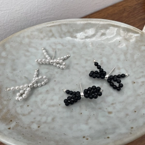 Detail view of handcrafted black and white beaded bow stud earrings on a ceramic dish