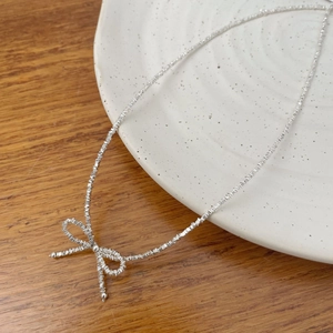 Macro detail of a silver bow knot necklace elegantly draped over a white ceramic plate
