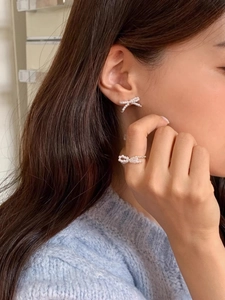 Detail of 925 silver pearl bow earrings and open ring on a model with blue sweater