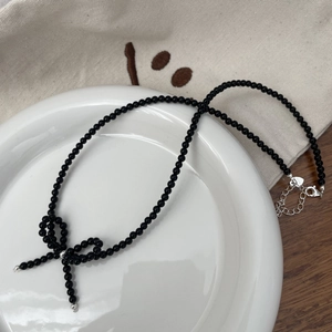 Detail of black beaded necklace with a woven bow pendant on white ceramic plate