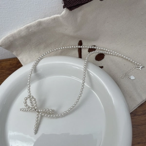 Macro view of white pearl necklace featuring a woven bow pendant and silver clasp