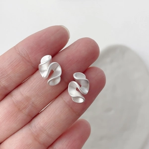 Dettaglio macro di orecchini in argento S925 con design ondulato opaco sulla mano