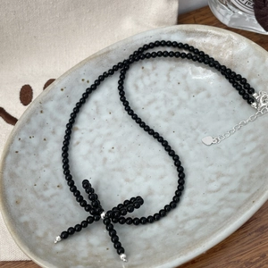 Detail of S925 sterling silver bow necklace with black beads on a ceramic tray