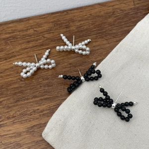 Detailed close-up of handmade beaded bow earrings in black and white styles on linen