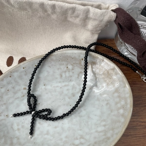 Detail of black beaded bow necklace with silver end caps on a minimalist ceramic plate