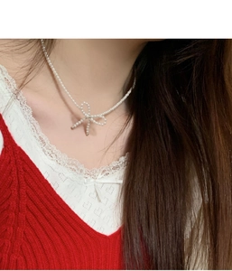 Detail view of a dainty pearl bow necklace worn on the neck for a sweet Korean style