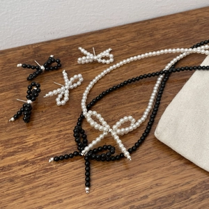 Detail of elegant pearl bow earrings and necklace set in black and white on wood surface